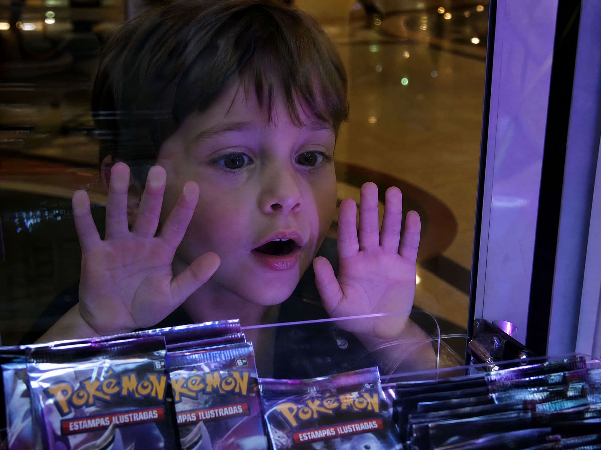 Criança com as mãos no vidro da máquina Rastro Collect, encantada com os boosters de Pokémon