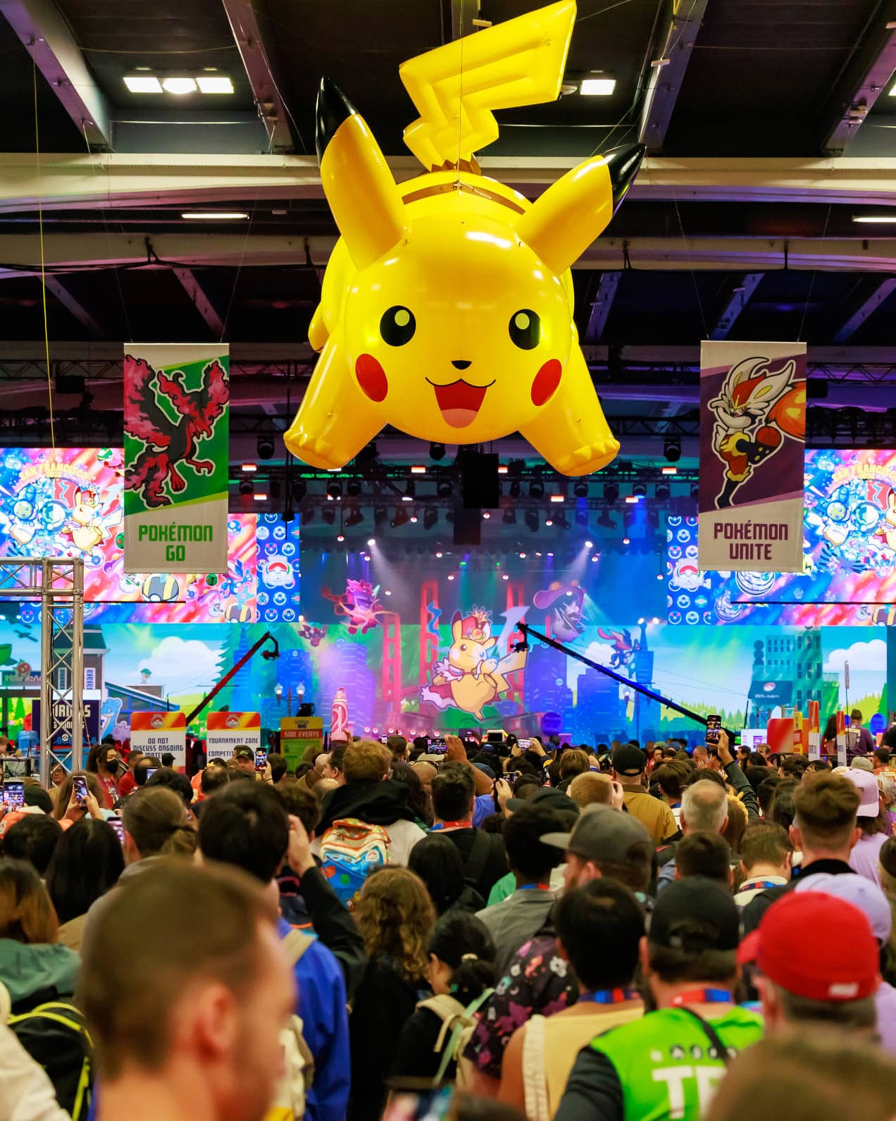 Multidão em um evento de Pokémon com um Pikachu inflável gigante sobre o público